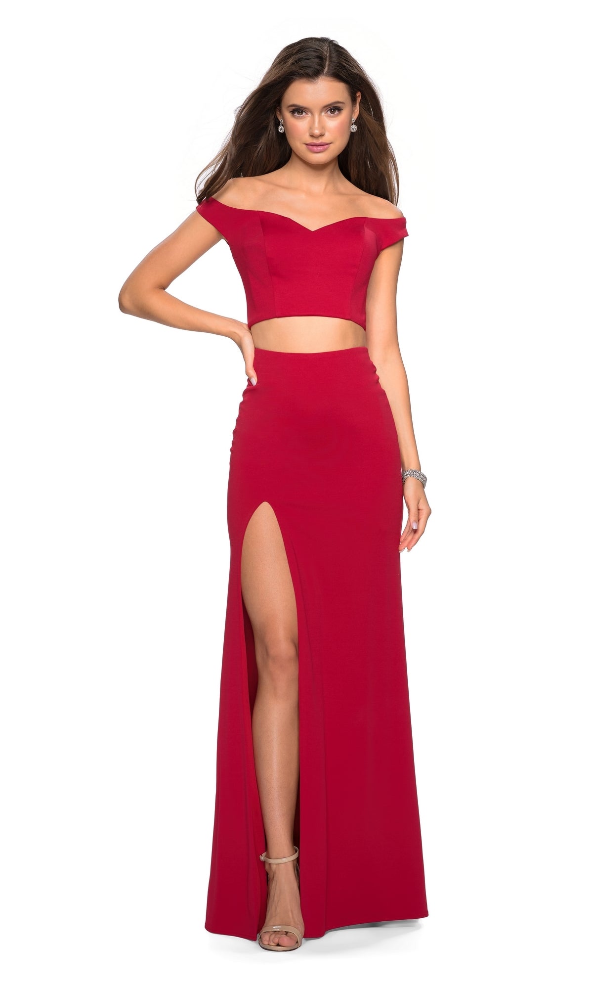A woman poses in the La Femme 27496 Off-Shoulder Two-Piece Prom Dress, a fitted red gown with a thigh-high slit, wearing heels and resting one hand on her hip.